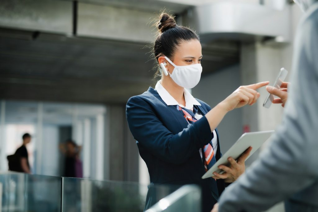 Flight attendant talking to businessman on airport, wearing face mask